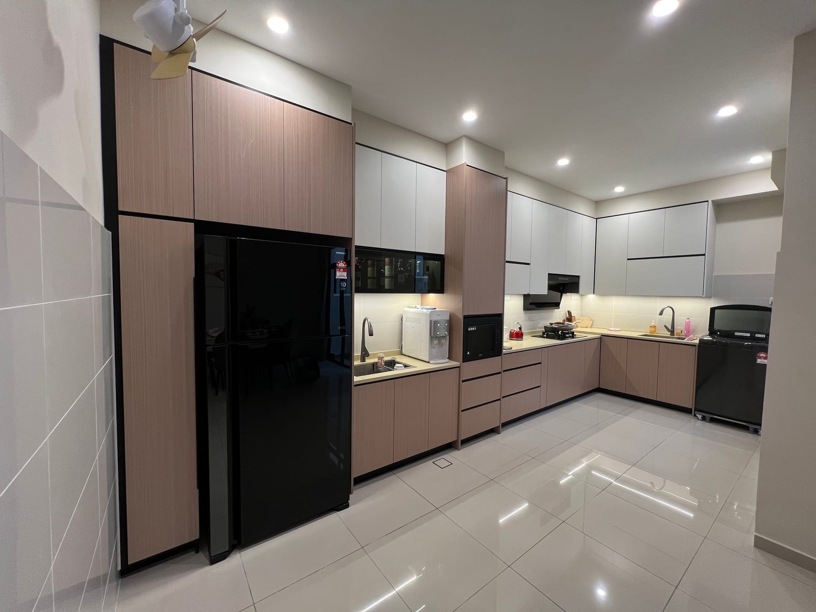 A completed fitted kitchen photographed across the whole run, with wood-grain tall units and white base cabinets.
